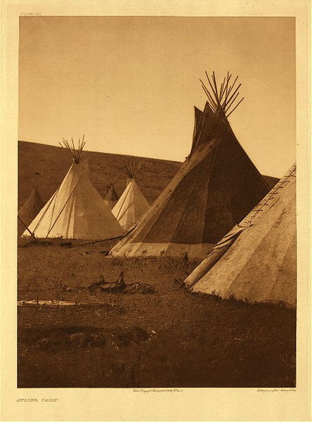 Edward S. Curtis - Plate 175 Atsina Camp - Vintage Photogravure - Portfolio, 22 x 18 inches - A great peak at what an Atsina camp looks like. The tipis are large and well-constructed. The composition of this photograph is interesting with the dark hill in the background creating an intersection with the triangular tipis. <br> <br>Description by Edward S. Curtis: The Atsina lived in tipis of twenty buffalo skins and twenty four poles, the latter about thirty feet in length. <br> <br>"It is believed that when a man dies he goes northward to 'Bashnobe,' the Big Sand, where he joins the spirits finds plenty of game and follows the customs and habits of their former existence. The ghosts of the dead are believed to haunt graves, to travel with the whirlwind, and to have the power of shooting invisible arrows into people." - From Edward Curtis' North American Indian