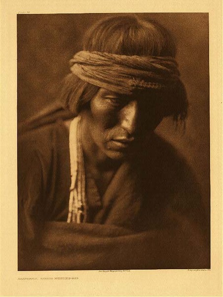 Edward S. Curtis - Plate 035 Hastobiga (Navaho Medicine Man) - Vintage Photogravure - Portfolio, 22 x 18 inches - Though it differs throughout tribes, there are many similarities in Native American Medicine. The primary function of most medicine men is to secure the help of the spirits. Sometimes this help may be sought to heal illness, psyche, or to promote harmony between people or nature. Medicine men are not necessarily doctors or herbalists in the way many think. They provide more of a bridge between spiritual worlds and the human world. <br> <br>Photographed by Edward S. Curtis in 1904, "Hastobiga" was a Navajo Medicine man. In this image he is wearing a headband and what looks like a brown robe. He looks as if he is deep in thought. His pensive expression is deepened by the photographer’s choice to keep half of his face in a deep shadow. <br> <br> From Edward Curtis' North American Indian. Originally an edition of 500 sets was proposed, but only 214 sets were subscribed to, and another 60 were compiled and sold later. One set belonged to fabulously wealthy railroad magnate Edward Harriman, another of Curtis' patrons. It was Harriman that financed the 1899 Alaska expedition for which Curtis served as the original photographer, and which would provide the inspiration and impetus for Curtis' magnum opus, The North American Indian. Harriman’s set is of the highest quality available, printed on Indian Proof Paper (tissue) tipped in, and Dutch Van Gelder paper.