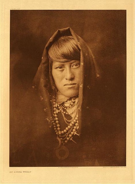 Edward S. Curtis - *50% OFF OPPORTUNITY* Plate 572 An Acoma Woman - Vintage Photogravure - Portfolio, 22 x 18 inches - In this photograph by Edward Curtis you see a young Acoma woman adorned with lots of jewelry including squash blossom necklaces. She is wearing a dark shawl and staring directly into the camera. Her hair is cut to have bangs. The photograph was manipulated by Edward Curtis to fade and is very artistically beautiful. <br> <br>"The Keres village of Acoma is the oldest continuously occupied settlement in the United States. Perched on top of a mesa some three hundred and fifty feet above the surrounding valley, accessible by difficult trails partly cut in the solid rock of its precipice, it is no less picturesquely placed than Walpi. Under the name Acus it was first mentioned by Friar Marcos de Niza, discoverer of the Zuni towns." from Edward S. Curtis' "The North American Indian", Volume XVI