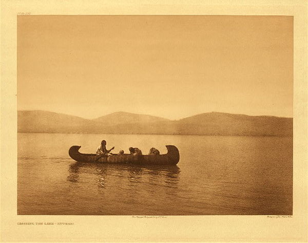 Edward S. Curtis - Plate 252 Crossing the Lake - Kutenai - Vintage Photogravure - Portfolio, 18 x 22 inches - Crossing the Lake was taken by photographer Edward S. Curtis in 1910. A tranquil scene of a few Kutenai rowing a beautifully built canoe to cross the lake. The Kutenai lived in mountainous areas with many lakes and thus became excellent boaters. The boat would be formed over a framework of split-fir and made of pine or spruce bark. Edward Curtis printed this piece on Japon Vellum and is available for sale in our Aspen Art Gallery.