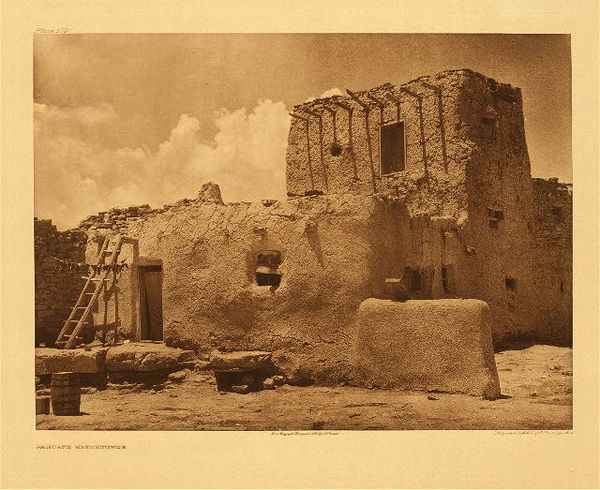 Edward S. Curtis - Plate 579 Paguate Watchtower - Vintage Photogravure - Portfolio, 18 x 22 inches - A Paguate Watchtower is a significant edifice. <br> <br>The oldest and largest of the outlying pueblos, equaling, if not slightly exceeding, Laguna in population is Paguate, separated from the mother pueblo by eight miles of difficult road and perched on a slightly elevated rocky eminence overlooking a small valley. The original Indian settlement at Paguate was an outpost established for the purpose of checking the Navaho. From Volume 16 of The North American Indian. <br> <br>This outpost is a stone structure built in three levels. The lower level was used for storing corn and wheat, the middle level was used for grinding the grains; and the upper level, accessible only by ladder, was used as a lookout and for protection of women and children during the Apache and Navajo raids. It was also used at times as a shelter for men and women who had journeyed for the day from the village of Laguna to farm the Paguate valley.