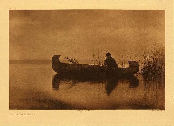 Edward S. Curtis - Plate 249 Kutenai Duck Hunter - Vintage Photogravure - Portfolio, 18 x 22 inches - The Kutenai Duck Hunter is one of Edward Curtis’ most iconic images, right alongside with Canon de Chelly or Bear’s Belly. The photo depicts a lone hunter, looking for ducks according o Edward Curtis “In the gray dawn of a foggy morning the hunter crouches in his canoe among the rushes, waiting for the water-fowl to come within range” from his North American Indian. The image is printed on Deluxe Japanese Tissue and is available for sale in our Aspen Art Gallery. <br> <br>"Inhabiting a mountainous country dotted with lakes and traversed by long winding rivers, the Kutenai very naturally became expert boatmen. The commoner form of craft was made of pine-bark or spruce-bark laid over a framework of split-fur. It was sharp at bow and stern, of a form still seen among the Kalispel." from Edward S. Curtis' "The North American Indian", Volume VII