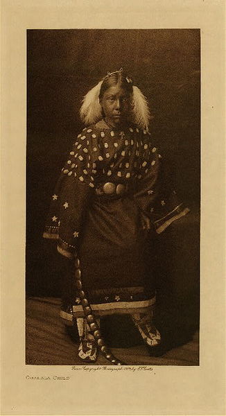 Edward S. Curtis - Ogalala Child - Vintage Photogravure - Volume, 12.5 x 9.5 inches - When a young woman gave her consent to marry her relatives would bring to her an elk-toothed dress, beaded moccasins, and leggings all of the things considered necessary for a married woman. The young Ogalala girl pictured here by Edward Curtis is wearing an example of the elk toothed dress and beaded moccasins that showed wealth and status in her tribe. <br> <br> This photogravure was taken in 1907 by Edward S. Curtis. The piece was printed on Dutch Van Gelder and is available for sale in out Aspen Art Gallery. <br> <br>Provenance: Original Subscription Set #59. George D. Barron, Rye, NY