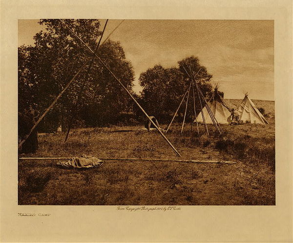 Edward S. Curtis - Making Camp - Vintage Photogravure - Volume, 9.5 x 12.5 inches - This photo by Edward S. Curtis depicts the process involved in building a camp for the Teton Sioux. After a perfect location is selected, here a place backed with a few trees for protection, they would begin setting up. The Sioux resided mainly in tipis and these were made of large poles which were then draped with buffalo skins. The tipis would allow for smoke to exit through the top using closable flaps. <br> <br> This photogravure was taken in 1908 by Edward S. Curtis. The piece was printed on Dutch Van Gelder and is available for sale in out Aspen Art Gallery. <br> <br>Provenance: Original Subscription Set #59. George D. Barron, Rye, NY