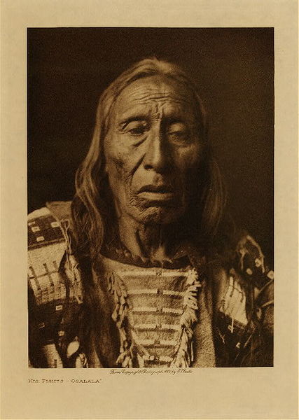 Edward S. Curtis - His Fights - Ogalala - Vintage Photogravure - Volume, 12.5 x 9.5 inches - Born 1832. At fourteen he accompanied a war-party under Long Bear and Buffalo Head against the Apsaroke. The ground was muddy, and the horses of the chiefs becoming exhausted, the warriors went on without their leaders. Arriving in the Crow country, they charged upon some hunters who were engaged in cutting up meat, killed and scalped two, and escaped with about ten horses. His Fights and the other boys guarded the clothing and extra horses of the warriors during this fight. When a young man, he went again against the Apsaroke. When the enemy was sighted, White Man's Fire, the medicine-man, donned his headdress of buffalo-horns and eagle-feathers, and while the chief held forward the war pipe he prayed, each of the warriors extending his own pipe toward the enemy. Then the medicine-man rode toward the war-pipe, which now lay on the ground, dismounted, and sat in front of it, while His Fights raised it and gave it to White Man's Fire, saying "Brother-in-law, go and tell the warriors what you have seen." A bit of buffalo-chip was placed on the top of the tobacco in the pipe and fire applied, after which the medicine-man smoked. Then he pointed with his thumbs and thrust one hand after another in the direction of the enemy, exclaiming "She! She!"-indicating that his heart was hot against them. "I see a hundred horses coming toward us. We will kill the Raven Men and one of them will be dressed like a chief." Then they charged, and succeeded in running off about eight hundred horses. The Apsaroke rushed out, and two boys and three men, one of the latter wearing a shirt covered with weasel-skins were killed. It was afterward learned that he was Big Otter. In the retreat twenty Sioux were killed and about half of the horses lost. No scalp dance followed the return of the party. His Fights' medicine was given him by White Man's Fire, who, in the summer preceding this fight, got it in the Black Hills, from a geyser which the medicine-man entered and from which he emerged holding several long white roots, one of which he gave to each of the five warriors present, at the same time instructing them how to paint. His Fights took part in the battle of the Little Bighorn. <br> <br>Provenance: Original Subscription Set #59. George D. Barron, Rye, NY