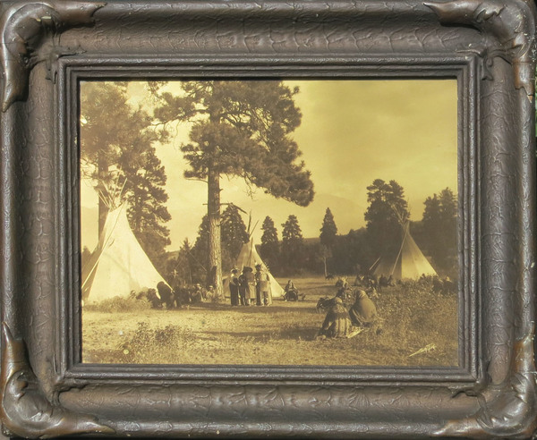 Edward S. Curtis - Flathead Camp on the Jocko - Vintage Goldtone - 11 x 14 inches - This incredibly rare goldtone depicts a small camp among the pines on the reservation of the Flatheads in western Montana. The majestic Rocky Mountains are rising abruptly in the background. Flatheads had no tradition of lodges other than the buffalo skin tipis you see pictured here. IT is a moody day and there are many Natives about camp. This goldtone is in the original frame and has the studio sticker intact. There is also price tag on the back from Curtis’ studio that says $5.00. Printed in 1910 this piece is now available for sale in our Aspen Art Gallery.