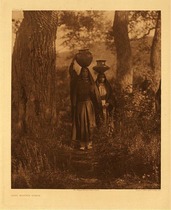 Edward S. Curtis - Plate 544 Taos Water Girls - Vintage Photogravure - Portfolio, 22 x 18 inches - Two Taos young women carry large water jugs upon their heads through the forest. Dressed in long dark dresses that drape all the way around their face. They have a clearly used path in a wooded area.
<br>
<br>The people of Taos, northernmost of all pueblos, and those of Picuris, a mountain village about 20 miles southeastward, speak the same tongue, a dialect of the Tiwa branch of the Tanoan stock language. - Edward Curtis