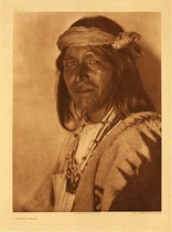 Edward S. Curtis - Plate 552 A Jemez Fiscal - Vintage Photogravure - Portfolio, 22 x 18 inches - An important man in the community this Jemez man is considered a “Fiscal”. His job requirements were like that of a governor and included supervising activities related to the church. He was in charge of such important matters as burial of the dead and the maintenance and care of the church itself.  While the Christian church was somewhat forced upon the Taos Pueblo people, it never became an integral part of life for them. The Spanish attempt to bring Christianity to the Native Americans in all tribes was generally a failed venture.
<br>
<br>In this photogravure by Edward Curtis the Jemez man and Fiscal looks directly into the camera. He is adorned with multiple necklaces and wearing a patterned cape. Often seen in Curtis’ images he is wearing a tied cloth bandana around his forehead. The background is light and is perhaps the side of an adobe structure.
