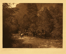 Edward S. Curtis - Plate 140  A Mountain Fastness - Apsaroke - Vintage Photogravure - Portfolio, 18 x 22 inches - Description by Edward S Curtis: The Apsaroke lived much among the mountains, and nowhere do they seem more at home than on the streams and in the cañons of their forested ranges.
<br>
<br>This images pictures a handful of men on horseback riding through a shallow creek. They are encompassed in trees and you can see a bit of the mountain that they are in the shadow of.
<br>
<br>In the old times the Apsaroke, during a large part of the year, were constantly on the move. One day they would be quietly encamped on one of their favorite streams, the next travelling away in quest of buffalo or solely for the mere pleasure of going. Their customary camps were along the mountain streams, where the lodges were commonly placed in a circle, but at times, where the valley was narrow, they were close together, paralleling the wooded watercourse.