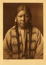 Edward S. Curtis - Plate 212 Cheyenne Girl - Vintage Photogravure - Portfolio, 22 x 18 inches - In this picture, taken by Edward Curtis in 1905, a young Cheyenne girl poses for the camera. She is wearing simple earrings, necklaces and a beaded ornamental garment. Her expression is skeptical with one eyebrow higher than the other. Her hair is in two long braids and he dress is quite simple.