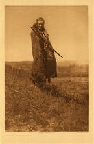 Edward S. Curtis - Plate 198 A Grizzly Bear Brave- Piegan - Vintage Photogravure - Portfolio: 22 x 18 inches - Like the famous portrait “Bears Belly” a Grizzly bear brave was also a member of the Grizzly-bear Braves. He wears a bear pelt and carries what is either a bow or a spear. Standing on a hill gives this piece a compelling composition and the subject’s intense stare is captivating. 
<br>
<br>Description by Edward Curtis: At least two of the Piegan Warrior societies (the Braves and the All Brave Dogs) included in their membership two men known as Grizzly-bear Braves. It was their duty, at the time of the society dances, to provide their comrades with meat, which they appropriated wherever they could find it. Their expression and demeanor did justice to their name, and in their official capacity they were generally feared by the people.