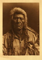Edward S. Curtis - Plate 229 A Flathead Chief - Vintage Photogravure - Portfolio, 22 x 18 inches - An elderly chief with his hair done in many braids stares questioningly in to the camera. The sideways light source shows his deeply wrinkled face and his garment appears to made of hide. He is holding some sort of gun and has a long bone necklace. 
<br>
<br>Flathead description by Edward Curtis: Through the medium of their annual incursions into the buffalo plains east of the Rocky Mountains, the Flatheads adopted much of the plains culture. Not only their domicile (the tipi), their garments, weapons, and articles of adornment, came from this source, but many of their dances were in imitation of similar ceremonies practiced by the prairie tribes. Prominent features of the accoutrement of this Flathead chief are his war-club of the plains type, and an eagle-bone whistle, such as was used in the Sun Dance. The Flatheads however never acquired the sun rite.