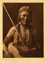Edward S. Curtis - Plate 142 Wolf - Apsaroke - Vintage Photogravure - Portfolio, 22 x 18 inches - Description by Edward S Curtis: Born 1857. Mountain Crow; Not Mixed clan; Fox organization. His medicine of wolf was obtained by purchase. He has to his credit a "dakshe" and a captured gun, both honors having been won at the same time, when he rushed into a protected hollow where were concealed two Yanktonai who had already killed three and wounded two of the attacking Apsaroke. Again, when a party of seven turned back without finding an enemy, Wolf alone went forward and captured a tethered horse from the camp. In pursuing some Yanktonai who had taken Apsaroke horses, he and a companion charged; his horse went down, and as he arose he himself was shot.
<br>
<br>This fabulous image of "Wolf" displays an elderly Apsaroke holding a long stick, probably a weapon of some sort. His hair suggests that he has won many scalps, or has done well in battle. He is wearing multiple necklaces as well as other interesting jewelry. Wolf is also painted with a white pigment and wearing a fur around his waist.