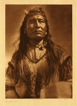 Edward S. Curtis - Plate 200 New Chest - Piegan - Vintage Photogravure - Portfolio, 22 x 18 inches - Pictured by Edward S. Curtis as if he was a Greek God, New Chest has a halo of light surrounding his strong facial features. Wearing traditional dress, but no headdress. Traditional dress for the Piegan would be deerskin clothing with ornamentation made from porcupine quills and beads made of silver-berry seeds. Of the Piegan tribe which means he could have been located in either Canada or Montana. This photogravure by Edward S. Curtis was printed in 1910 on Dutch Van Gelder paper. It is now available for sale in our Aspen Art Gallery.