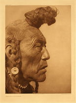 Edward S. Curtis - *50% OFF OPPORTUNITY* Plate 640 Bear Bull - Blackfoot - Vintage Photogravure - Portfolio, 22 x 18 inches - Edward Curtis captures a fascinating aspect of North American Indian lifestyle. The hair worn in this manner is very specific to the Blackfoot tribe. The elder men allow their hair to grow, and twist it in the same manner as the Assiniboines; but instead of forming the coil on the crown, they wear it on the forehead, projecting seven or eight inches in a huge knob, smeared with red earth.
<br>
<br>A simple yet stunning portrait of a Blackfoot man named, “Bear Bull”. Pictured in profile one can see the deeps lines of a long life in his face. With a braided bun atop his forehead, he displays the ancient Blackfoot method of doing hair. The Blackfoot were fierce enemies and this man likely has seen many battles. Taken by Edward S. Curtis in 1927 this image is on display in our Aspen Art Gallery.
