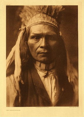 Edward S. Curtis -   Plate 262 Nez Perce Warrior - Vintage Photogravure - Portfolio, 22 x 18 inches - This close up image of a Nez Perce Warrior displays a unique looking headdress. The subject has one eyebrow raised in a questioning expression. He is wearing a necklace of shell and a brown vest over a white shirt.
<br>
<br>"The Nez Perces were a loosely associated group of local bands, each possessing its own territory and own chief. It is true that they had a collective name for these bands, and that there were occasions when perhaps the greater part were in one camp, as at the camps meadows or during fall fishing in the Wallowa and the Salmon. Nevertheless there was in reality no tribal organization. The bands were kindred, spoke the same language, and associated for mutual defense; but they remained distinct." - Edward Curtis
