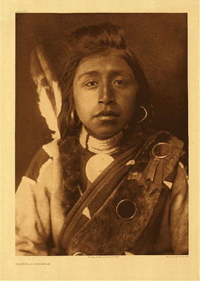Edward S. Curtis -   Plate 283 Kashhila - Wishham - Vintage Photogravure - Portfolio, 22 x 18 inches - 	Description by Edward S. Curtis: "This sturdy young fellow has little of the appearance of the Chinookan. In feature and in costume he recalls the plains Indian."
<br>
<br>By using a solid background and shooting this portrait from the waist-up, Curtis is directing the viewer to focus solely on the Wisham sitter, specifically their expression and dress. In their youthful face, the mood is imperceptible and enigmatic with their relaxed features and gaze.