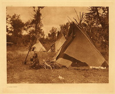 Edward S. Curtis - Plate 620 A Sarsi Camp - Vintage Photogravure - Portfolio, 18 x 22 inches - This photogravure by Edward Cutis has two people, a woman by the cooking fire, and a man stands in the back with an ornate cloak.
<br>
<br>In Volume 18 Edward Curtis writes - The Sarsi are a small Athapascan tribe that separated, before the historical period, from the Beaver Indians. The Sarsi mythological explanation this that a large body of people were migrating southward across a frozen lake, the ice was suddenly shattered by a water-monster whose horn had been frozen in it, and those who had already crossed were the ancestors of the Sarsi.
<br>
<br>This tribe originally resided in the Saskatchewan, but migrated near and became closely associated with the Blackfeet, Bloods and Piegan and were often considered a fourth member of that confederacy and adopted many of the material and religious customs. Nevertheless, they preserved their own language.
