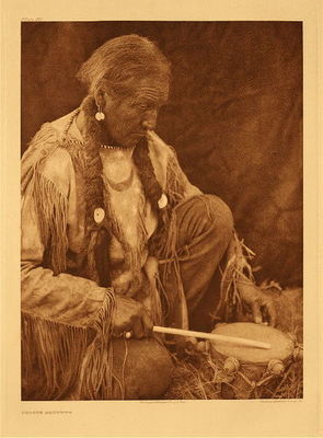 Edward S. Curtis - *50% OFF OPPORTUNITY* Plate 687  Peyote Drummer - Vintage Photogravure - Portfolio, 22 x 18 inches - Regarding the Peyote Ceremony the leader, in prayerlike recital tells the story of peyote. “We are assembled in a sacred lodge for the worship of the Divine Ones; we know the Wakoda created all things, animal and plant. We know that He Himself created Peyote. Believing this, we know that He created it for our use, for our good. We know that we should not look upon Peyote as medicine, nor worship it as an idol, but rather regard it as a symbol of Wakoda, our Creator. We know that our minds, our thoughts, should be upon spiritual things while worshipping in this lodge.”
<br>
<br>After the peyote is ingested, the Leader addresses the member in words of admonition: “Remember the sacred nature of the meeting. Remember that we are worshipping Wakoda as instructed by him.”
<br>
<br>The leader, accompanied by the drummer, next chants the four sacred songs, meanwhile holding a staff and a wisp of sage in his left hand, and, in his right hand, a rattle with which he accompanies the chant.
<br>
<br>This worshipful time is followed by the Water Ceremony, which celebrates the earth, “Our Mother.” The song ends, the leader speaks, telling his followers of Wakoda’s creation of day, the coming of the sun; that through the spirit of water they have life. With the closing words he places the staff and rattle on the alter.