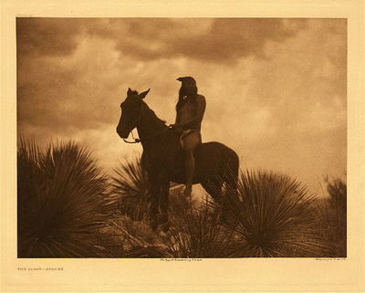 Edward S. Curtis - Plate 013 The Scout-Apache - Portfolio, 18 x 22 inches - "No people could be better fitted than the Apache to conduct continuous predatory warefare. Every form of plant and animal life pays him tribute. An entirely naked Indian, without implements of any sort, would stop on a mountain slope and in a few minutes be sitting by a cheerful fire preparing a welcome meal. With a fragment of stone he would shape fire-sticks from the dead of a yucca. Sitting with the flattened piece held firmly by his feet, a pinch of sand at the point of contact between the two sticks, with a few deft whirls of the round stick over his improvised hearth the lone traveller would soon have a fire kindled."