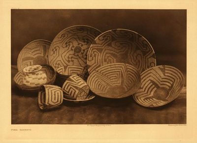 Edward S. Curtis - Plate 041 Pima Baskets - Vintage Photogravure - Portfolio, 18 x 22 inches - The baskets made by the Pima, Papago, and Qahatika, as well as by their Maricopa neighbors, are almost identical in form and design. As captured in this image, the four-armed cross, a form of the swastika, appears as the central feature in the decoration of a majority of the Piman and Maricopa baskets. Although the true significance of this iconography is not known with certainty, it is theorized that the pattern originally represented the winds of the four cardinal directions. The swastika was also employed by the Pima to decorate their shields, and as a brand for their horses.