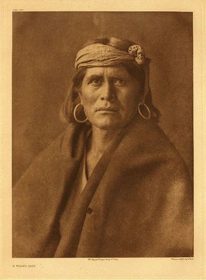 Edward S. Curtis -   Plate 424 A Walpi Man - Vintage Photogravure - Portfolio, 22 x 18 inches - Wrapped in a thick brown shawl this Walpi man has a strong and somber expression. He looks directly at the viewer and is almost fully lit. An interesting haircut, this man has a short cut while we are used to seeing longer hair on Native Americans, especially of this age. He is wearing hoop earrings and has a piece of cloth ties around his head. Of the Walpi tribe this man would have lived in present day Arizona.
<br>
<br>"The religious and ceremonial life of the Hopi centers in the kiva, which is simply a room, wholly or partly subterranean and entered by way of ladder through an opening in the flat roof...While the membership of the kiva consists principally of men and boys from certain clan or clans, there is no case in which all the members of a kiva belong to one clan - a condition inseparable from the provision that a man may change his kiva membership, and in fact made necessary by the existence of more clans than kivas. It is probable; nevertheless, that originally the kivas were clan institutions." - Edward Curtis