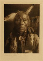 Edward S. Curtis -   Struck by Crow - Ogalala - Vintage Photogravure - Volume, 12.5 x 9.5 inches - Born 1847. At eleven he accompanied a party against the Apsaroke, the one in which Fast Thunder served as a warrior. He participated in ten battles, most of them against the Apsaroke, and fought four times against troops, three of these occasions being the Fetterman massacre, the engagement with Crook's command at the Rosebud, and the battle of the Little Bighorn. Counted coup twice, both in the same fight, when twenty Flathead and two Sioux were killed. Fasted four times in the Bighorn Mountains and experienced a vision. Early in the morning he took five tanned buffalo-skins to the summit and gave them to Mystery. He remained on his feet until long after darkness had fallen, and then as he laid sleeping he saw the fork of a river, and beside it a ridge over which came many horses driven by a man. Some of the horses were white. The next day at sunset he returned to his camp and went into the sweat-lodge. A short time after this Struck By Crow accompanied a raiding party and captured some white horses.
<br>
<br>Provenance: Original Subscription Set #59. George D. Barron, Rye, NY
