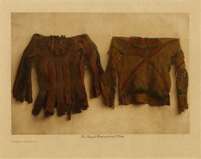 Edward S. Curtis - *50% OFF OPPORTUNITY* Scalp-Shirts - Vintage Photogravure - Volume, 9.5 x 12.5 inches - "The important article of dress for those who has won the necessary honors to warrant them in wearing it was the scalp- or honor shirt- a coat-like garment fringed at the bottom as well as along the side-seams and sleeves, and slipped on over the head. In making the scalp-shirt two deerskins of medium size were placed together face to face, sewn at the shoulders, and tied at the sides. The sleeves were sewn firmly at the shoulders and left open along the under side of the arms. The garment was ornamented with beadwork on body and sleeves, and, according to the owner's deeds of valor, with tufts of human hair, weasel-skins, and feathers, each component part of this decoration telling its own story of the wearer's prowess. When taking a scalp, a warrior often removed almost the entire head-covering of the enemy; this was divided into many small pieces for use on the scalp-shirts. The hair of white people was not used for this purpose, as the taking of their scalps was not considered an honor" by Edward S. Curtis in "The North American Indian", Volume III
<br>
<br>This image was taken by Edward Curtis in 1908 and handpainted.
<br>
<br>Provenance: 
<br>Art Institute of Chicago, Ryerson & Burnham Library