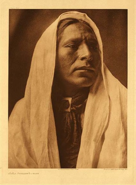 Edward S. Curtis - Plate 545 Lahla ("Willow") - Taos - Vintage Photogravure - Portolio, 18 x 22 inches - This handsome Taos man has strong Native American features framed by a white draping around his head. Looking off to the side and slight upwards this man looks as if he is longing for something, perhaps the past. The lighting is ethereal giving him an almost god-like appearance. Contrasted by the dark brown background, this portrait stands out as one of Edward S. Curtis’ finest works.