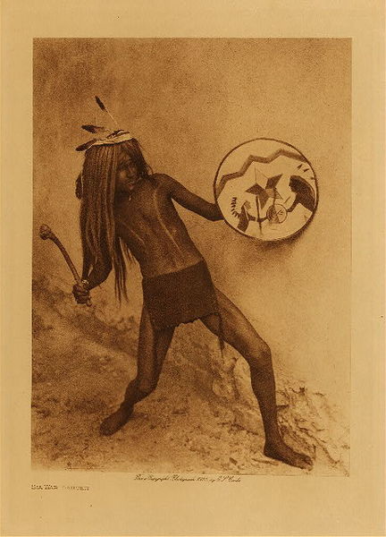 Edward S. Curtis - *50% OFF OPPORTUNITY* Sia War Dancer - Vintage Photogravure - Volume, 12.5 x 9.5 inches - In the Sia tradition those who had taken scalps were formed into a society. A war party returning from a raid would have a sort of victory dance where singing and celebration would ensue. The celebrations would last for four days, a scalp ceremony was also a portion of this. On the fourth day the war-dance occurred. Pictured here by Edward Curtis is one of the war dancers, wearing a small loincloth and holding a decorated shield. <br> <br>This photogravure was taken in 1926 by Edward S. Curtis. The piece was printed on Japon Vellum and is available for sale in out Aspen Art Gallery.