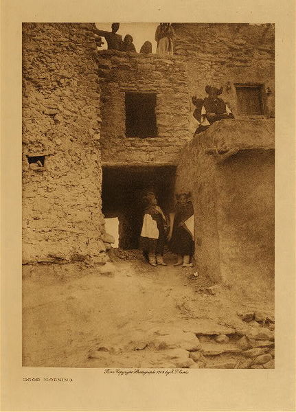 Edward S. Curtis - Good Morning - Vintage Photogravure - Volume, 12.5 x 9.5 inches - This Edward S. Curtis photo depicts a morning scene in a Hopi village. There are young girls in traditional dress and hair and it is a great example of the complex apartment-like buildings they created for themselves. This photogravure was taken by Edward Curtis in 1906 and is printed on Japon Vellum. The piece is now available for sale in our Aspen Art Gallery.