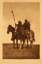 Edward S. Curtis -   Plate 172 Atsina Chiefs - Vintage Photogravure - Portfolio, 22 x 18 inches - In this image two Atsina Chiefs are riding strong horses. One carries a long stick adorned with feathers which is perhaps a Coup stick. The picture was taken from below so that the chiefs looks extremely large and important. We also get a full view of the entire horse and rider.<br><br>Edward S. Curtis' description from,  "The North American Indian”: "The Atsina, commonly designated Gros Ventres of the Prairie, are of the Algonquian stock and a branch of the Arapaho. Their name for themselves is "Aaninen," Atsina being their Blackfoot name. Judging by their vague tradition, their original separation from the Arapaho must have occurred in early times; but care should be taken not to confuse with this primal separation their return to the north from an extended visit to the Arapaho during the last century."<br><br>"The tribe was composed of ten bands, all under one head, who with the chiefs of the bands, formed the council. The head-chief conducted treaties on the part of the tribe, selected camp sites, and directed tribal affairs generally. When he and the council disagreed, two young men, each representing a faction, were sent out with a bundle of sticks. passing around in the camp in opposite directions they stopped at each sub-chiefs lodge and asked what side of the question he favored....having completed the circuit of the camp, the two young men returned to the head-chief's lodge, the decision of those represented by the messenger with the fewest sticks....."