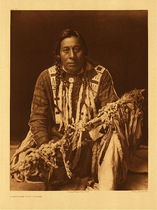 Edward S. Curtis -   Plate 199 A Medicine Pipe - Piegan - Vintage Photogravure - Portfolio, 22 x 18 inches - Curtis' Description: Medicine-pipes, of which the Piegan have many, are simply long pipe-stems variously decorated with beads, paint, feathers, and fur. Each one is believed to have been obtained long ago in some supernatural manner, as recounted in a myth. The medicine-pipe is ordinarily concealed in a bundle of wrappings, which are removed only when the sacred object is to be employed in healing sickness, or when it is to be transferred from one custodian to another in exchange for property. Such exchanges, occurring at intervals of a few years in the history of each pipe, are attended by much ceremony