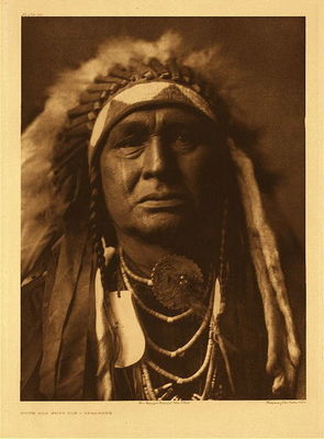Edward S. Curtis -   Plate 115 White Man Runs Him (One of Custer’s Crow Scouts) - Vintage Photogravure - Portfolio, 22 x 18 inches - Born about 1854 or 1855. Mountain Crow; Big Lodge clan; Lumpwood organization. His only coup was counted by the capture of a tethered horse. Noted for his many successful horse-raiding expeditions against the Sioux. <br>Scouted with Custer in his last campaign, and was one of the party of three or four scouts who, at the dawn of the morning of the Custer fight, first sighted the Sioux camp. A small party of Crow and Arikara scouts under Lieutenant Varnum, having traveled nearly all night, arrived shortly before dawn almost a the summit of the highest peak in the Wolf mountains, where the party slept for a short time. At approaching light White Man Runs Him and a couple of companions went to the top of the high peak which gave them the first view of the Sioux encampment. Following Custer's coming up to view the valley and its camp of hostiles, he was with Custer until the Sioux made their attack on him. White Man Runs Him's recollections of that day are exceedingly clear. The author spent several days with him traveling carefully over the ground covered on the day of the disastrous fight on the Little Bighorn, part of this time being accompanied by general C.A. Woodruff. <br>White Man Runs Him possesses no medicine derived from his own vision, but once fasted four days and four nights in the Bighorn mountains on a peak known to the Apsaroke as "Where White Man Runs Him Fasted." Of his seven wives he gave up six "good ones," that is, those who had borne him children; to discard such was an indication of a strong heart.