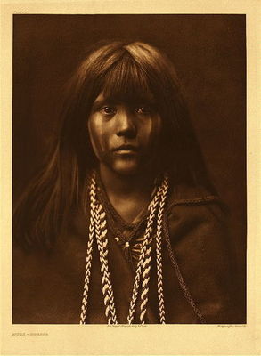 Edward S. Curtis -   Plate 061 Mosa - Mohave - Vintage Photogravure - Portfolio, 22 x 18 inches - “It would be difficult to conceive of a more aboriginal than this Mohave girl. Her eyes are those of the fawn of the forest, questioning the strange things of civilization upon which it gazes for the first time. She is such a type as Father Garces may have viewed on his journey through the Mohave country in 1776.”<br><br>The Mohave tribe was one of the most primitive; from their method of hunting, to lack of curiosity to see past where they lived, “along the backs of the Colorado river, an environment into which they have so fitted themselves that they seem to have been always a vital part of it. To describe the Mohave without first speaking of their river would be like telling of the Makah of wind-swept Cape Flattery without alluding to the sea that beats the sands at their very feet.”<br><br>This quiet, simple life shows on the face of Mosa – there is no cynicism, or defiance. There is only the look of a young girl who is looking into Curtis' lens with the emotion and power that the photographer captured beautifully.