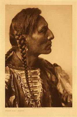Edward S. Curtis -   Plate 149 Spotted Bull - Mandan - Vintage Photogravure - Portfolio, 18 x 22 inches - from Volume V in "The North American Indian" by Edward S. Curtis:<br><br>"No more impaired than the Mandan material culture were their religious and ceremonial beliefs and practices. Nothing had yet shaken their faith in their own gods. As the bird instinctively builds its own nest to meet its own needs, the Mandan had formulated their religion to fit the requirements of their life, and were strong in precepts. Their well developed political organization enabled them to execute effectively the tribal laws.<br><br>The society organization of the Mandan is worthy of particular notice. The system comprised seven societies, or lodges, though which a man passed successively, beginning with the Fox order. The usual age of entrance into this grade was eighteen to twenty years, and no one younger than fifty years was permitted to enter the Bull society, the sixth organization of the system. To become a member of this system one had first to purchase the rights of a member of the lowest order before passing successively through the others. This could not be done individually, but only when it was arranged that the whole society purchase the right of the next highest one."