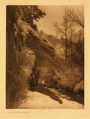 Edward S. Curtis -   Plate 132 Passing the Cliff - Vintage Photogravure - Portfolio, 22 x 18 inches - A winter scene on Pryor Creek, Montana<br><br>The country which the Apsaroke ranged and claimed as their own<br>was an extensive one for so small a tribe. In area it may be compared,<br>east and west, to the distance from Boston to Buffalo, and north to<br>south, from Montreal to Washington — certainly a vast region to<br>be dominated by a tribe never numbering more than fi fteen hundred<br>warriors. The borders of their range were, roughly, a line extending<br>from the mouth of the Yellowstone southward through the Black<br>Hills, thence westward to the crest of the Wind River mountains,<br>northwestward through the Yellowstone Park to the site of Helena,<br>thence to the junction of the Musselshell and the Missouri, and down<br>the latter stream to the mouth of the Yellowstone. This region is the<br>veritable Eden of the Northwest. With beautiful broad valleys and<br>abundant wooded streams, no part of the country was more favorable<br>for buffalo, while its wild forested mountains made it almost unequalled<br>for elk and other highland game.