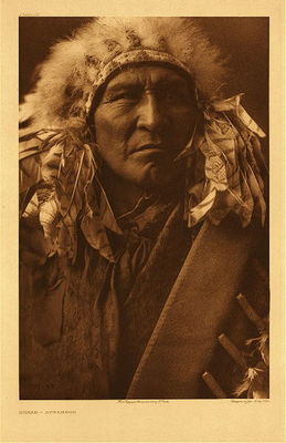 Edward S. Curtis -   Plate 121 Bread - Apsaroke - Vintage Photogravure - Portfolio, 22 x 18 inches - Born 1863. A Mountain Crow, (he was a member of the) Whistle Water clan. First war experience under Young Wolf Calf, when the party captured a hundred horses from the Piegan. On another occasion, under Wet, he himself captured a horse from the Yanktonai. Married five times; "threw away" four wives; is the father of one child. Never fasted and never achieved an honor.<br><br>The Apsaroke were and are the proudest of Indians, and although<br>comparatively few, they rarely allied themselves with other tribes for purposes of defence. For probably two and a half centuries they were the enemy of every tribe that came within striking distance, and for a goodly part of this time they were virtually surrounded by hostile bands with a common hatred against this mountain tribe that likened itself to a pack of wolves. The swarming thousands of the western Sioux, aided by the Cheyenne and Arapaho, tried to force them westward. The powerful Blackfeet invaded their territory from the north and northwest, Flatheads and Nez Percés were worthy foes from the west, and the wily Shoshoni pressed in from the south; yet the Apsaroke were ever ready to repel invasion from whatever direction it might come.