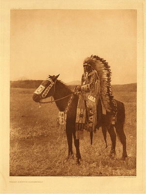 Edward S. Curtis -   Plate 629 Chief Hector - Assiniboin - Vintage Photogravure - 22 x 18 inches - Chief Hector, the son of Spotted Calf.<br><br>Three centuries ago, the seven divisions of the Dakota were dwelling in the region between the headwaters of the Mississippi and the west end of Lake Superior. About the time of the landing of the Pilgrim Fathers, a band of the Yanktonai, deserting their tribesmen in anger, says tradition, over wrong done to the chief's wife, moved away to the north and east, until, after indefinite wandering, they established a temporary home on the shores of a wooded lake. Thus, the Assiniboin tribe was born, first mentioned as distinct from the Dakota by the Jesuit Relation of 1640 on "Lake Alimibeg," later identified as either Rainy lake on the northern boundary of the present state of Minnesota, or else Lake Nipigon, north of Lake Superior in the direction of Hudson Bay.
