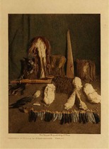 Edward S. Curtis - *40% OFF OPPORTUNITY* Contents of Bundle of Numak Mahana - Mandan - Vintage Photogravure - Volume, 12.5 x 9.5 inches - The contents of this bundle include a girdle of buffalo skin with many strands of twisted hair hanging off, a large wooden pipe inlaid with stone, a cimeter-shaped club of ash ornamented on one side with carved figures of the moon and the thunderbird, a stuffed Raven, a headdress of porcupine hair, a collar and anklets of jack rabbit skin, a bunch of four buffalo tails, a set of buffalo teeth, and more. <br><br>All of this paraphernalia is held and protected by a man named Packs Wolf a priest of the tribe. This photograph was hand colored and printed by Edward Curtis in 1909. It is now on display in our Aspen Art Gallery.