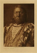 Edward S. Curtis -  *40% OFF OPPORTUNITY* Charge Crow - Yanktonai - Vintage Photogravure - Volume, 12.5 x 9.5 inches - Born near Standing Rock in 1850. When in his seventeenth year he joined a war party against the Apsaroke near the Little Bighorn, the Yanktonai capturing a number of horses. While fighting the Flatheads, Charge Crow killed one and took his horse. He led a war-party on foot, and encountering the Atsina near Fort Belknap, Montana, captured fifty horses. Having found an old police badge, he visited a camp of Cree and told them he was an officer. They believed him, and Charge Crow stole most of the horses in the camp, and got away with them safely. Although he fasted often and prayed to the sun, he never had a vision; he attributes his success in war to the potency of his prayers. He married at twenty-one.<br><br>The Yanktonai are known to have resided in North Dakota and Montana until reservation days and the total population in Curtis time was around 6,500.<br><br>Charge Crow frowns into the camera in this image, he is dressed traditionally. This photogravure was taken in 1908 by Edward S. Curtis and is now available at our Aspen Art Gallery.<br><br>Provenance: Original Subscription Set #59. George D. Barron, Rye, NY