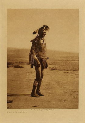 Edward S. Curtis -   White Man Runs Him (Full Figure) - Vintage Photogravure - Volume, 12.5 x 9.5 inches - Born about 1854 or 1855. Mountain Crow; Big Lodge clan; Lumpwood organization. His only coup was counted by the capture of a tethered horse. Noted for his many successful horse-raiding expeditions against the Sioux. <br><br>Scouted with Custer in his last campaign and was one of the party of three or four scouts who, at the dawn of the morning of the Custer fight, first sighted the Sioux camp. A small party of Crow and Arikara scouts under Lieutenant Varnum, having traveled nearly all night, arrived shortly before dawn almost the summit of the highest peak in the Wolf mountains, where the party slept for a short time. At approaching light White Man Runs Him and a couple of companions went to the top of the high peak which gave them the first view of the Sioux encampment. Following Custer's coming up to view the valley and its camp of hostiles, he was with Custer until the Sioux made their attack on him. White Man Runs Him's recollections of that day are exceedingly clear. The author spent several days with him traveling carefully over the ground covered on the day of the disastrous fight on the Little Bighorn, part of this time being accompanied by general C.A. Woodruff. <br><br>White Man Runs Him possesses no medicine derived from his own vision, but once fasted four days and four nights in the Bighorn mountains on a peak known to the Apsaroke as "Where White Man Runs Him Fasted." Of his seven wives he gave up six "good ones," that is, those who had borne him children; to discard such was an indication of a strong heart.<br><br>Provenance: <br>Art Institute of Chicago, Ryerson & Burnham Library