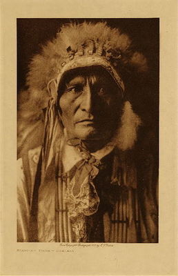 Edward S. Curtis -   Standing Bear - Ogalala - Vintage Photogravure - Volume, 12.5 x 9.5 inches - Men wore hip high leggings, loin cloth and moccasins, all made from tipi-coverings softened by weathering and by long exposure to smoke. Customarily no shirt was worn, when necessary, being covered with a buffalo skin belted at the waist. The war-bonnet of eagle feathers arrayed in a circlet about the heat and extending in a flowing train even to the heels was worn on special occasions by the warriors.  Women wore deerskin dresses reaching half-way below the knee, with elbow length sleeves open at the armpits and tied with thongs. Leggings extended from ankle to knee, and moccasins were ornamented with quill work.<br><br>Provenance: <br>Art Institute of Chicago, Ryerson & Burnham Library